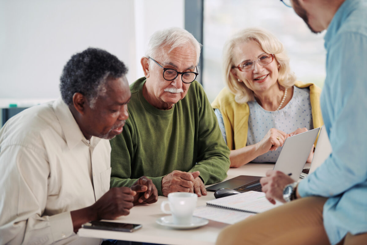 Older adults gathered around a table, discussing information on a tablet during a small group learning conversation.